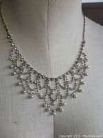Clear rhinestone bib necklace displayed on a mannequin, showing front view with cascading rhinestones and faux pearl drops.