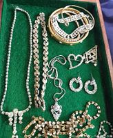 Top view of costume jewelry pieces on green cloth showing bracelets, necklaces, pins, and earrings with rhinestones