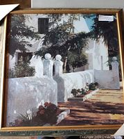 Framed square art print showing a white stucco outdoor setting with shadows and flower beds, framed in gold tone.