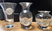 Three clear crystal vases with Princess House Exclusive stickers, different shapes, on a wooden surface.
