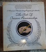 Front cover of the workbook showing the title 'The Art of Cursive Penmanship' by Michael R. Sull with ornamental design and a hand holding a pen illustration.