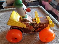 Side view of vintage Fisher-Price Jalopy toy car showing clown driver, vibrant orange wheels, yellow trunk lid and windshield frame, and detailed lithographed body