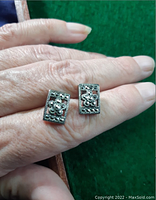 Pair of rectangular sterling silver earrings on hand showing detailed raised flower design and beaded edges.