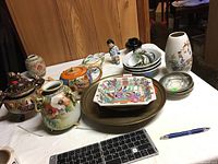 Wide shot of Asian ceramic collection showing teapots, plates, vase, cups, saucers, and figurine on table.