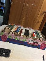 Photo showing a cardboard box labeled for fresh produce with 13 books inside, arranged upright with spines visible