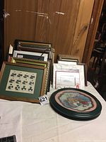 Stack of small framed pictures and empty frames against wood-paneled background.