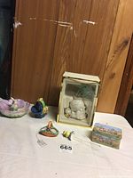 Overview of seven Easter-themed figurines and collectibles including Lenox cat figurine in box, small Easter chicks, bunny bowl, and painted trinket box on a white surface against wood panel background.