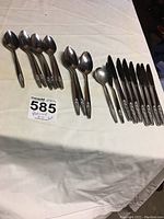 Full set of flatware laid out on linen cloth including tablespoons, knives, and spoons.
