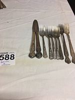 Photo showing 6 floral patterned silverplate dinner forks and 2 butter knives on white fabric background.