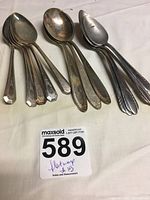 Photo showing three sets of spoons with different handle designs resting on a white surface next to a lot number card.