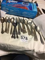 Full view of 14 assorted vintage spoons laid out in two groups showing a variety of handle designs and sizes.