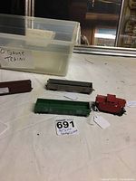 Overall view of two open box cars and one caboose with an unidentified brown box car and plastic storage bin labeled HO Gauge Trains.