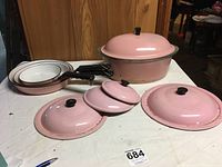 Set of pans and lids arranged on a surface showing broiler and three smaller pans in retro pink color.