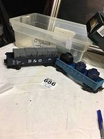 O gauge open box cars with containers inside, placed near a clear plastic storage box.