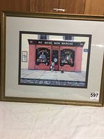 Framed print of Paris doll store with gold frame and double mat under glass, showing storefront, child, and dog