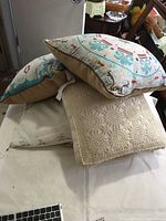 Set of four pillows stacked showing embroidered, crocheted, and plain small embroidery pillows on white surface