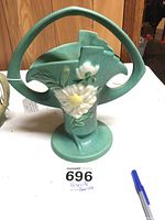 Front view of bluish green Roseville pottery vase with floral relief and large handle