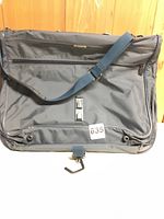 Front view of the blue Samsonite garment bag showing shoulder strap and external pockets.