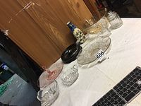 The overall lot items arranged on a white cloth table; includes multiple glass and ceramic pieces plus wooden nut dish with pickers and blue pottery bottle.
