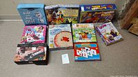 Photo of all 9 board games arranged on floor showing titles and box artwork for identification