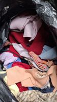 Photo showing bag filled with assorted wool fabric scraps in various colors and textures including red, pink, blue, and beige.