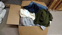 Box containing various linen fabrics including blankets and sheets of different colors and textures.