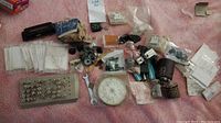 Full lot overview with various electrical and ham radio parts spread on a pink surface including connectors, fuses, meter and small parts.