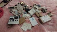 Overview of electrical and ham radio components scattered on pink cloth including meters, tubes, circuit elements, boxes, and accessories.
