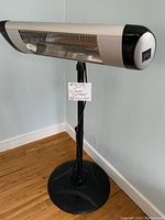 Full view of electric indoor/outdoor T heater on black adjustable stand with circular base on wooden floor.