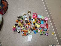 Full lot of mixed action figures and toys spread on floor including princess dolls, Barbie accessories, Paw Patrol figures, and various cartoon figurines.