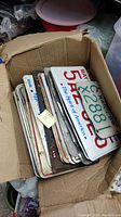 Box full of miscellaneous vintage license plates stacked inside, showing different designs and conditions