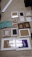 Photo showing 15 picture frames in a variety of colors and styles arranged on a carpeted floor, some without backing stands.