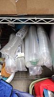 Stacks of clear plastic portion cups and lids wrapped in plastic on a metal shelf.
