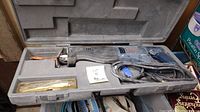 Ryobi reciprocating saw inside the open hard plastic case with compartment for saw, power cord, and extra blades.