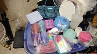 View of multiple Tupperware containers and lids, some bagged, in various colors and sizes on top of a large blue plastic bin.