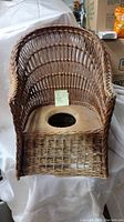 Full view of the wicker potty chair, showing curved backrest, armrests, and wooden seat with the hole.