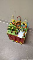 Full view of the wooden busy zoo activity cube showing the top bead maze and front wooden panels with animal motifs.