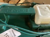 Close-up of the green Bissell steam cleaner with the white water tank and power cord.