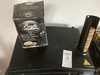 Black Bradley electric smoker top view showing side chimney filled with bisquettes and unopened box of Special Blend bisquettes