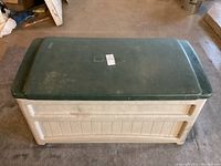 Closed green lid on beige plastic deck storage box showing some marks and wear.