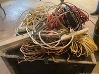 Photo showing a pile of coiled extension cords in multiple colors (yellow, orange, red, white) with attached surge protectors featuring multiple outlets, coiled and stacked on a black box.