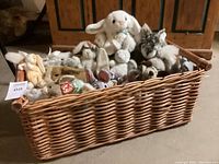 Wicker IKEA basket filled with various plush stuffed animals, viewed from front side showing multiple rabbits and other animals.