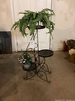 3-tier black iron plant stand assembled with artificial plants placed on tiers in open space