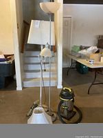 Photo showing two standing lamps with white lampshades, an extra white lampshade on the floor, and a Stanley vacuum cleaner in front of them.
