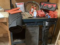 Full view of garage workbench holding multiple tool and garage items, including chainsaw bar and chain, axle stands, tool bags, mats and more.