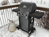 Full front view of the Sterling barbecue grill with one propane tank placed beside it on the snowy deck.