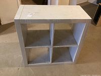 White storage cube with four compartments shown from front angle, visible surface wear and scuff marks, placed on a concrete floor.