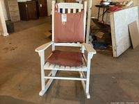 White painted wooden rocking chair with red cushions on seat and backrest, shown front view.