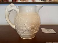 Side view showing the dog-shaped handle and hunting scene relief on the cream-colored Wedgwood pitcher.