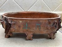 Front side view of the oval pottery dish showing Chinese characters and feet shaped like natural wood elements.